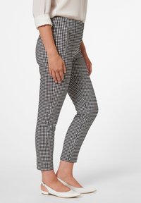 Pantalons à motif vichy noir et blanc avec une coupe slim, dotés de poches latérales zippées et d'une texture de tissu lisse.