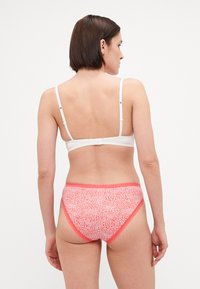 Hvit BH med justerbare stropper, kombinert med rosa mønstrede truser med en teksturert design og kontrastkant langs kantene.