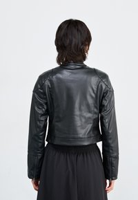 Veste de moto en cuir noir avec un design court, des épaules structurées et des poignets zippés, associée à une jupe noire à taille élastique.