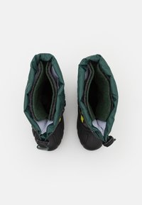 Botas aisladas negras con una parte superior elástica verde y acentos amarillos. El interior cuenta con un forro suave y texturizado para mayor abrigo.