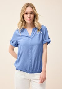 Blusa azzurra a maniche corte realizzata in tessuto morbido, con scollatura a V e risvolti, dotata di orlo arricciato per una vestibilità comoda.