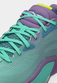 Κοντινό πλάνο αθλητικού παπουτσιού σε τιρκουάζ και μοβ χρώμα με κορδόνια σε τυρκουάζ, άνω μέρος από δίχτυ, μαξιλαρωμένη γλώσσα και υφή στην πλαϊνή επιφάνεια.