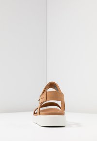 Sandalo in suede tan con suola bianca, dotato di cinturini regolabili e design piatto. Stile minimalista, che mette in risalto dettagli di cucitura e una texture morbida.