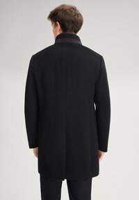 Cappotto di lana nera con colletto e una singola apertura sul retro. Presenta una texture liscia e una lucentezza sottile. Design pulito e semplice.