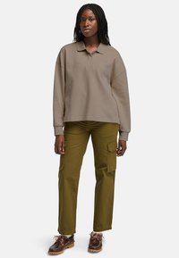 Světle hnědá oversized polo košile s límečkem, doplněná olivově zelenými cargo kalhotami se bočními kapsami. Hnědé boty s tkaničkami.