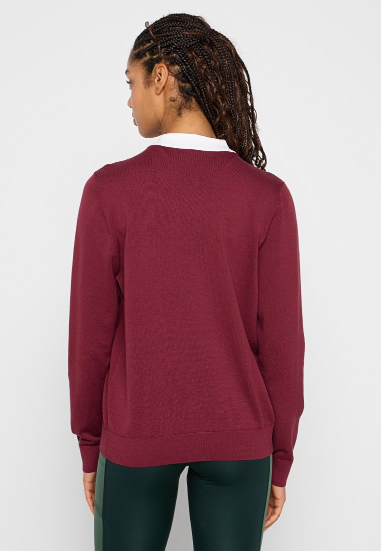 Bordeauxroter Pullover mit strukturiertem Rippmuster, langen Ärmeln, rundem Ausschnitt und weißem Kragenbesatz, kombiniert mit dunkelgrünen Leggings.