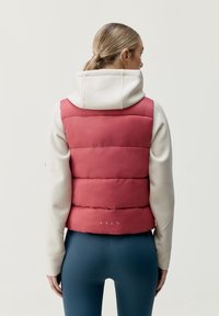 Fitted rosa puffer-väst med horisontella segment, ihopparad med en krämfärgad hoodie. Har en något kortad design och en mjuk yta.