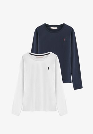 Dos camisetas de manga larga: una blanca con un pequeño logo negro, y la otra azul marino con un pequeño logo rojo. Ambas tienen escote redondo y tela suave.