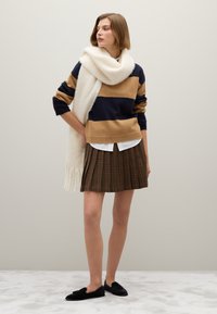 Gestreifter Pullover in Marineblau und Beige, weißer Schal, karierter Faltenrock in dunklen Tönen, schwarze flache Schuhe, neutraler Hintergrund, weiche Textur.