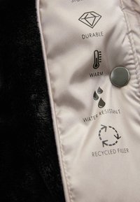 Sort faux fur-stof med lyse satinfor viser plejeikoner for holdbarhed, varme, vandmodstand og genanvendt fyld.