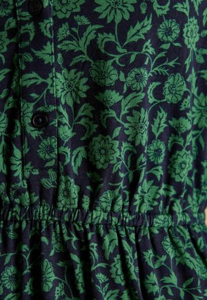 Tamsiai mėlyna medžiaga su žaliais gėlių raštais, mygtukais ir susiraukšlėtos juostos detale. Minkšta tekstūra su lapų ir žiedų motyvais.
