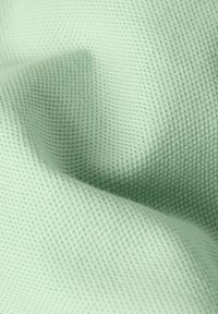 Ljusgrön texturerad tyg med ett våffel-liknande mönster, med mjuka veck och en slät yta, som skapar ett lätt utseende.