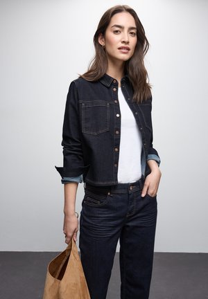 Tumma denimpuku cropped-takki kahdella etutaskulla, napitus edessä ja vaaleansiniset hihansuut. Yhdistetty tummiin farkkuihin ja vaaleanruskeaan anteeksi suede-laukkuun.