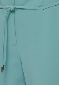 Lichtblauwe broek van zachte stof, met een elastische tailleband met metalen uiteinden en een gladde textuur. Inclusief zijzakken.