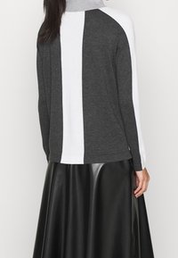 Vrouw die een lange mouw turtleneck sweater met verticale witte en donkergrijze strepen en een zwarte leren rok draagt, gezien van achteren.