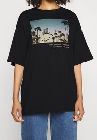 Czarny, oversize'owy t-shirt wykonany z bawełny, z nadrukiem graficznym przedstawiającym palmy i kosz do koszykówki oraz tekstem "Venice Beach, Kalifornia."