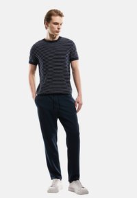 Navy gestreiftes T-Shirt mit kurzen Ärmeln, kombiniert mit navy Jogginghosen und weißen Sneakern. Glatter Stoff, lockere Passform, einfaches Design.