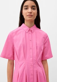 Sukienka koszulowa z krótkim rękawem i kołnierzykiem w intensywnym różowym kolorze, z przodem na guziki i plisowanymi detalami, wykonana z gładkiej bawełny.