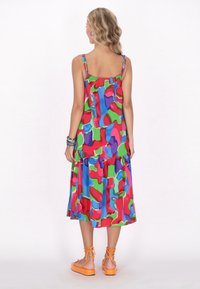 Rochie midi colorată, cu un design stratificat, prezentând modele abstracte în nuanțe vii de roșu, albastru, verde și mov. Bretele subțiri ajustabile și tiv volănat.
