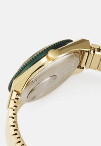 Montre dorée avec un cadran vert, boîtier rond et bracelet métallique à maillons. Couronne située sur le côté, dos affichant une surface lisse.