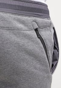 Grey athletic pants with a textured finish, featuring a contrasting waistband, side zipper pocket, and a soft fabric for comfort.