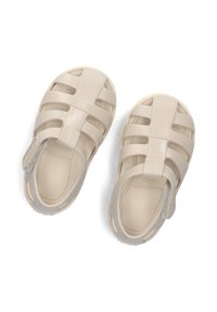 Beige plastic sandals with a closed toe and strappy design. Features a back strap and textured sole for grip.