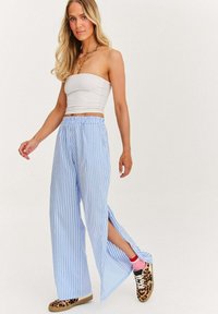 Světle modré a bílé pruhované kalhoty s širokými nohavicemi a bočními rozparky, kombinované s bílým topem a vzorovanými teniskami. Hladká textura látky.