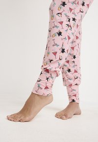 Mallas rosas con un patrón divertido de pingüinos y cócteles. La tela parece suave y elástica, diseñada para la comodidad.