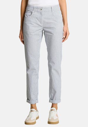 Kobieta nosząca jasnoniebieskie i białe pionowo prążkowane spodnie podwinięte u kostek, w białych i beżowych trampkach.