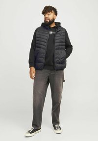 Schwarze Pufferweste über einem schwarzen Hoodie, kombiniert mit grauen Jeans und Converse-Sneakern. Die Weste verfügt über einen Reißverschluss vorne und ein gestepptes Design.