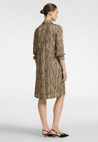 Vestido de estampado animal en marrón con mangas largas, puños abotonados y cuello. De longitud hasta la rodilla y con un corte holgado. Se lleva con zapatos de tacón marrones.