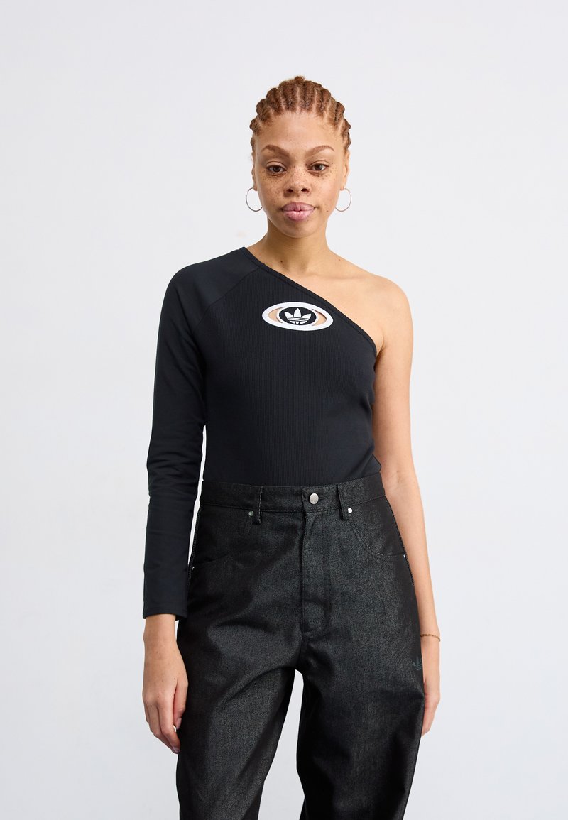 Svart en-skulder bodysuit med lang arm, prydet med en rund flerfarget logo på brystet, kombinert med høytaljede mørke denimbukser.