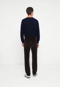 Pull marin à col rond, associé à un pantalon en velours côtelé marron foncé. La tenue présente une coupe décontractée et une texture subtile.