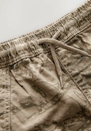 Tarnmuster-Shorts in Beigetönen mit einem Kordelzugbund und einem weichen, strukturierten Stoff, der Falten und Nähdetails aufweist.