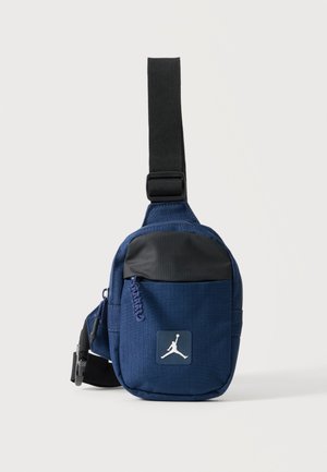 Kis kék-fekete válltáska elülső cipzáras zsebbel és állítható fekete pánttal, elöl fehér Jumpman logóval.