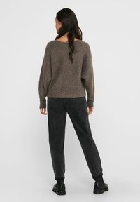 Pull en tricot marron avec une coupe décontractée et des poignets côtes, associé à un jean noir fuselé et des bottines. Vue arrière.