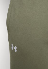 Olivgrüne Sportshorts aus weichem Stoff, mit einem kleinen weißen Logo an der unteren Seite. Einfaches, schlankes Design.