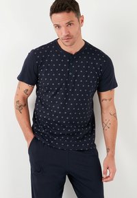 Camiseta de manga corta azul marino con cuello redondo, que presenta un patrón de diamantes y dos botones azules en el cuello. Tejido suave con un ajuste casual.