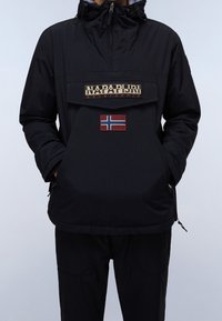 Sort hætteanorak med en frontlomme, der prydes af et logo og et norsk flagmærke. Fremstillet af glat, letvægtigt stof.