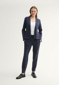 Blazer bleu marine avec une coupe ajustée, un bouton unique et deux poches avant, associé à un pantalon à cordon assorti et à des chaussures noires.