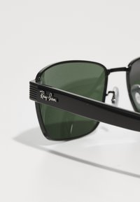 Ochelari de soare Ray-Ban negri cu lentile verde închis, formă rectangulară, braț texturat și logoul argintiu pe lateral.