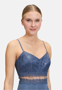 Bralette en dentelle bleue ornée de sequins, avec des bretelles réglables et une bande transparente agrémentée de motifs floraux complexes.