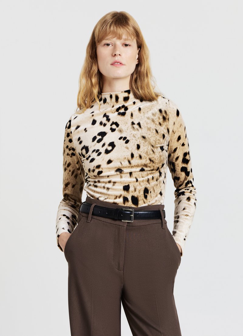 Maglia a maniche lunghe con collo alto in morbido velluto stampato con motivo leopardato beige e nero. Abbinata a pantaloni marroni a vita alta e cintura nera.