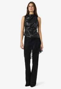 Svart ärmlös topp i glansigt läder med texturerad drapering, ihop med en genomskinlig spetskjol med asymmetrisk design över åtsittande svarta byxor.