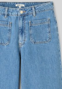 Jean large bleu clair en denim. Présente une taille haute, un design à cinq poches et des coutures visibles le long des coutures.