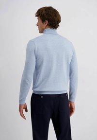 Lichtblauwe pullover met een hoge kraag en geribde mouwen, gecombineerd met marineblauwe broek met twee achterzakken en ronde hardware-accenten.