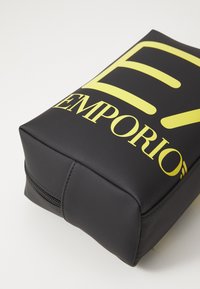 Bolsa preta com fecho zíper e uma textura suave; apresenta grandes letras amarelas "EMPORIO" e um design abstrato da letra "E".