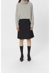 Maglione grigio con collo a cappuccio, gonna nera a campana, calze nere a coste fino al ginocchio e ballerine nere a punta. Design semplice e casual con texture morbide.