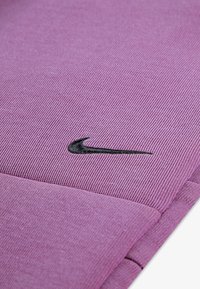 Ρούχο Nike σε απαλό μωβ ύφασμα, με υφασμένο σχέδιο. Στην επιφάνεια υπάρχει μαύρο κεντημένο λογότυπο, που προσθέτει αντίθεση.