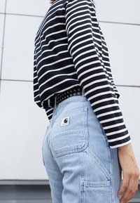 Camisa de rayas azul marino y blanca de manga larga combinada con vaqueros azul claro que presentan un parche de logo de marca y un cinturón negro con tachuelas.